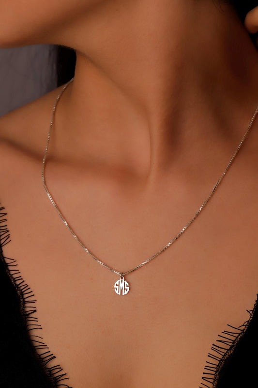 A close-up image of a sterling silver monogram necklace with a tiny initial pendant on a box chain, worn by a person.