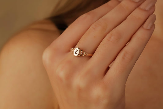 Rose gold ring with a letter 'E' on a hand against a neutral background