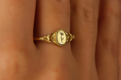 A gold-colored ring with an engraved floral design, displayed on a person's finger.