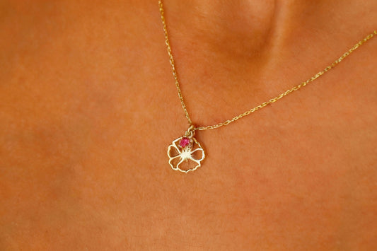 Gold necklace with a flower pendant on a person's neck against an orange background