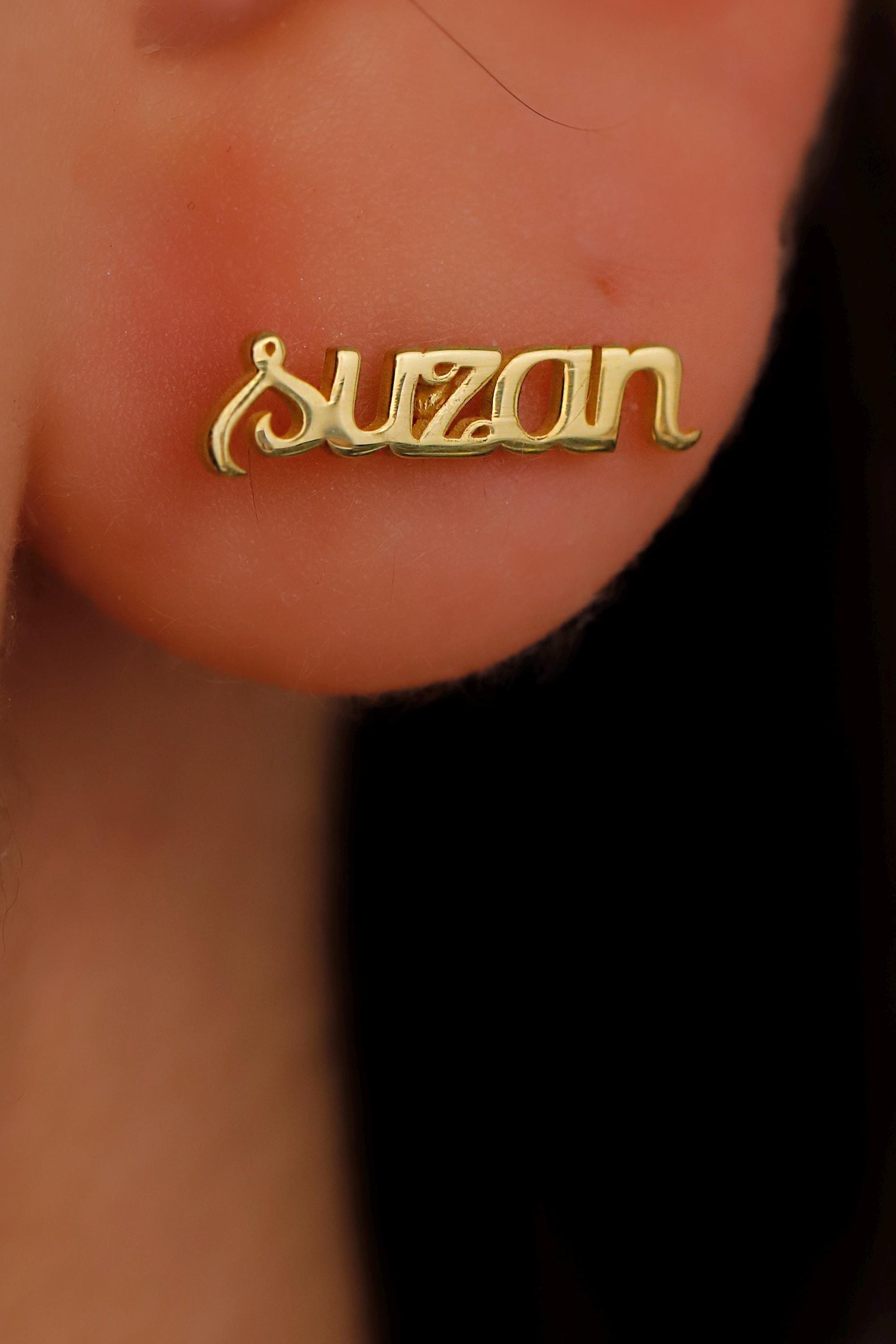 Gold 'Suzan' nameplate earring on a person's ear.