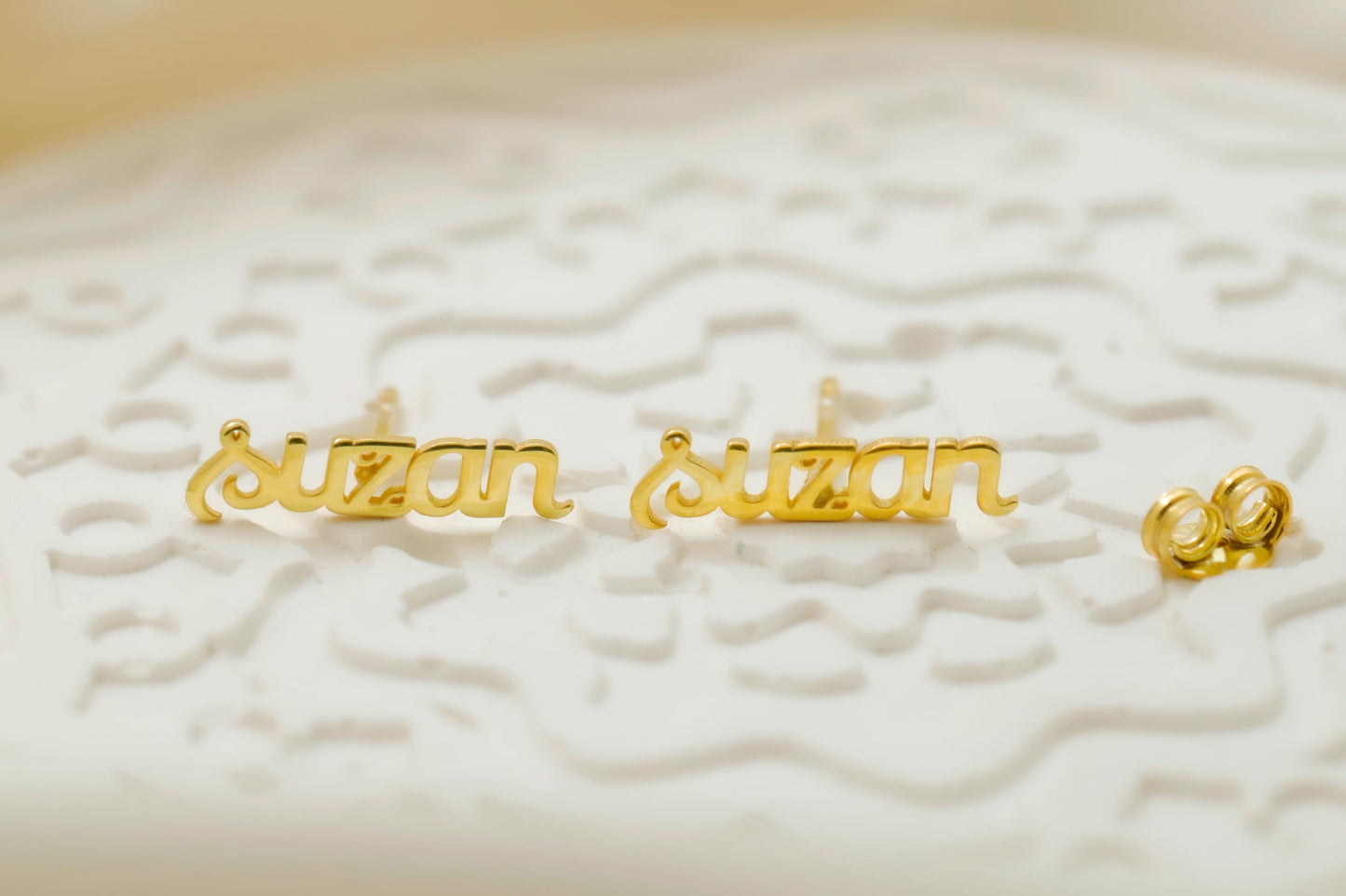 Gold 'susan' nameplate earrings on a textured white surface