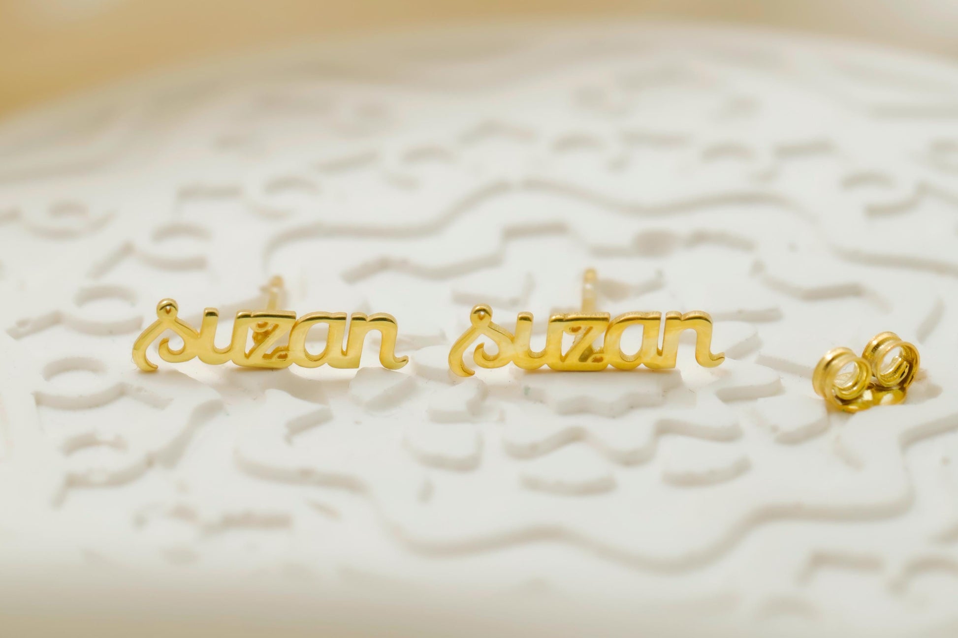 Gold 'susan' nameplate earrings on a textured white surface