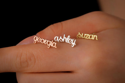 Gold name rings on a hand with a dark background