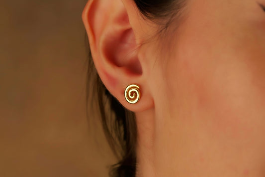 Close-up of an ear wearing a gold spiral earring against a neutral background