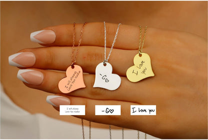 Three heart-shaped necklaces with engraved messages on a hand.