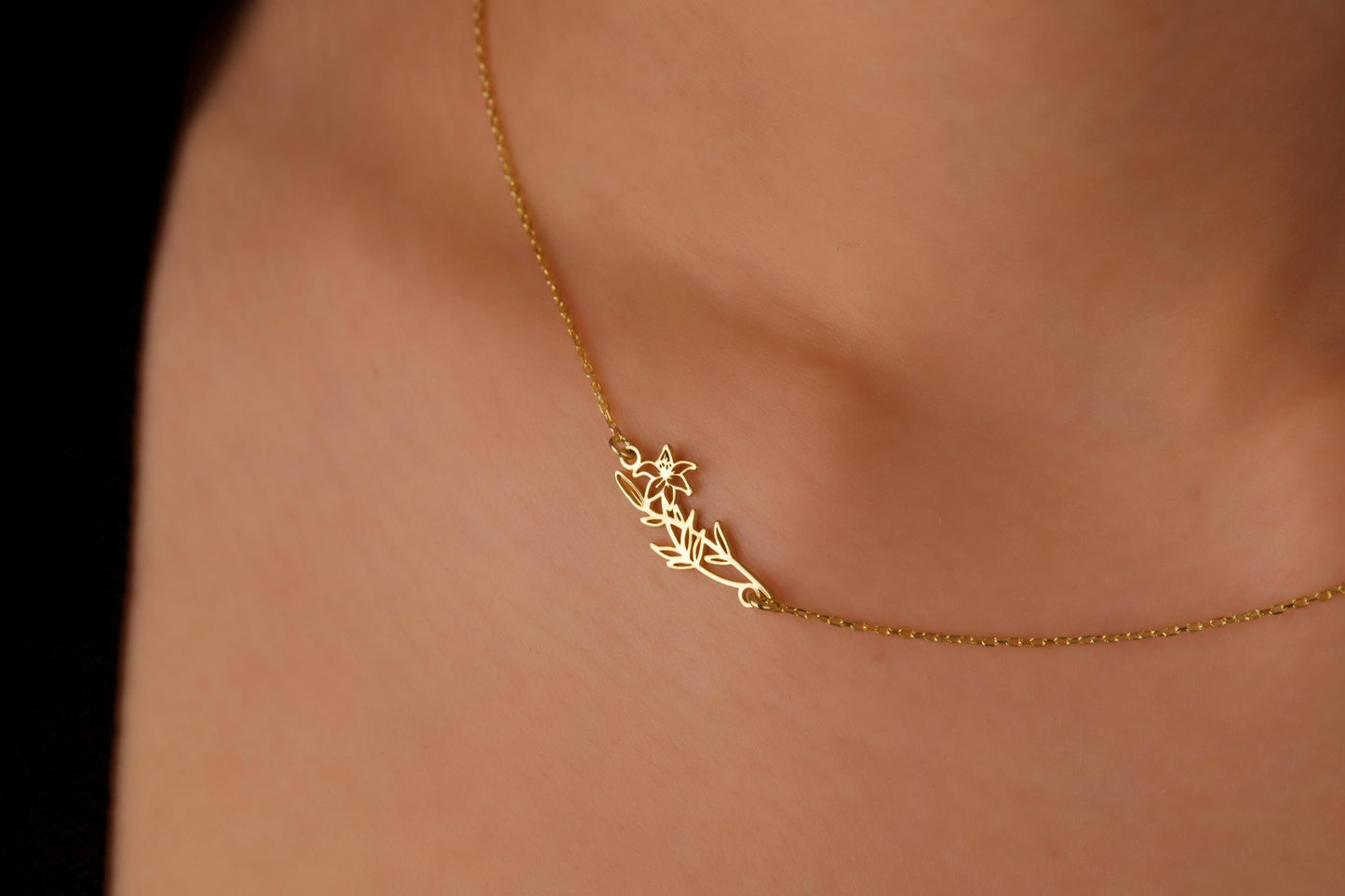 Gold necklace with a leaf design on a person's neck against a black background