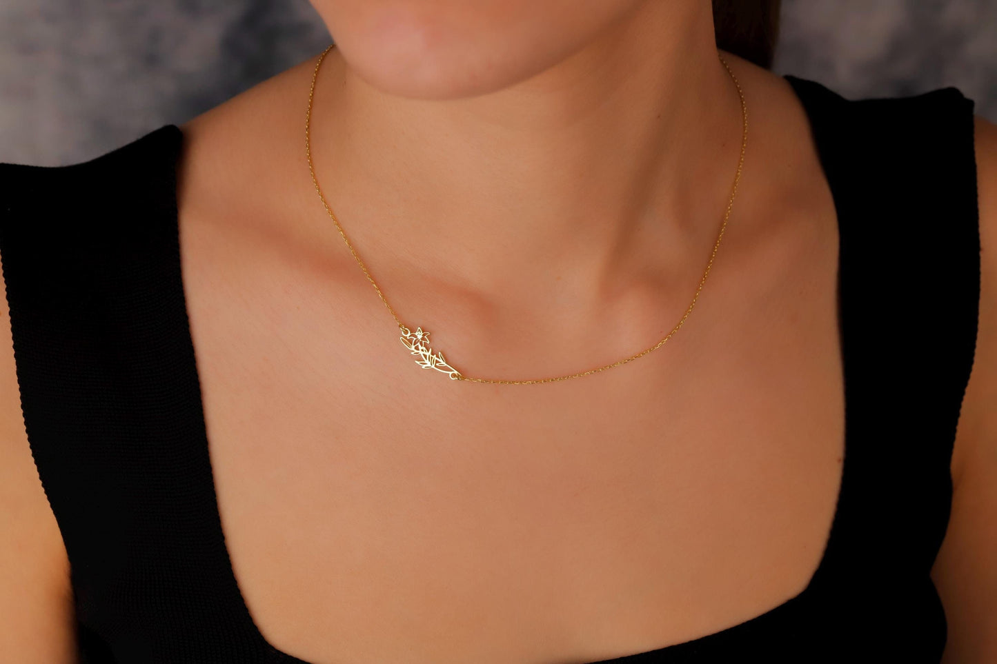 Gold necklace with a leaf design worn by a person against a neutral background