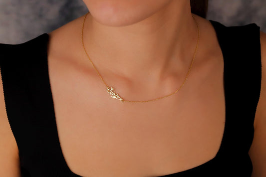 Gold necklace with a leaf design worn by a person against a neutral background
