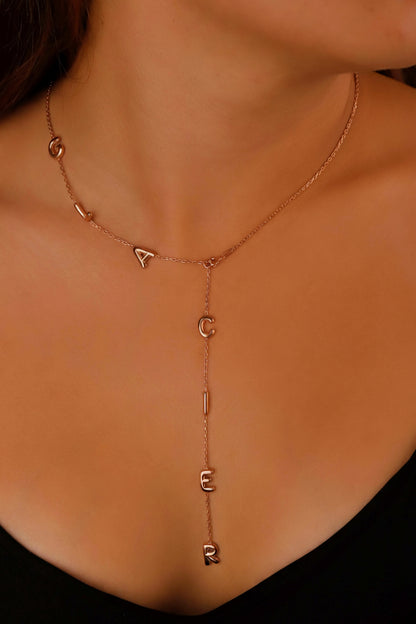 Rose gold necklace with letter pendants on a person wearing a black top.