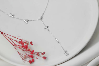 Silver necklace with geometric pendants on a white surface with red dried flowers.