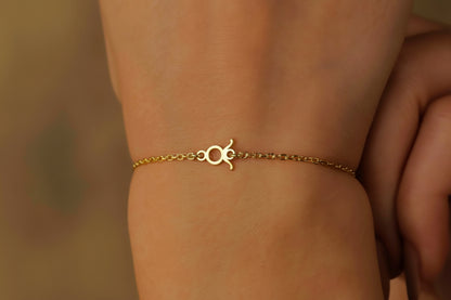 A gold-colored bracelet with a zodiac sign charm on a person's wrist.