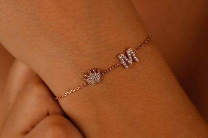 A  dainty bracelet worn on a wrist, featuring initials and crown charms with cubic zirconia stones.