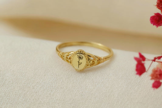 Gold ring with floral design on a beige surface with red flowers