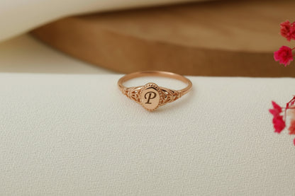 Rose gold ring with 'P' on a beige fabric background