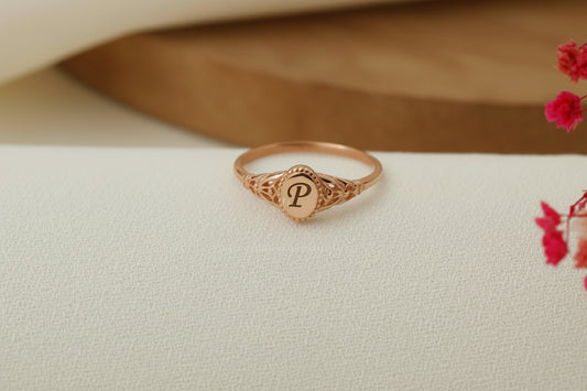 Rose gold ring with 'P' on a beige fabric background