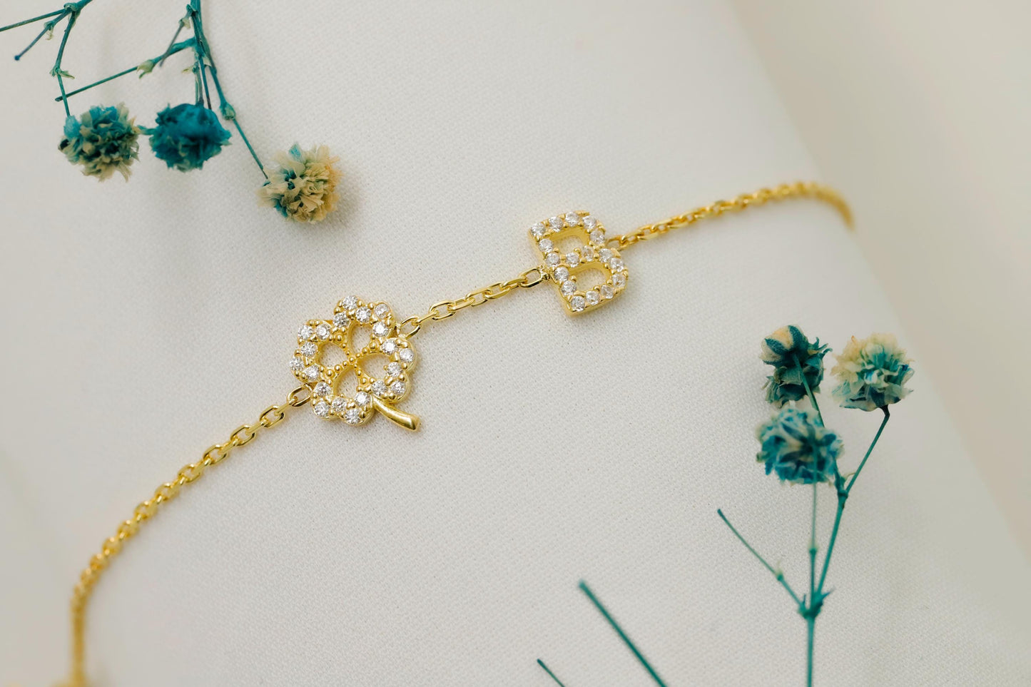 Gold bracelet with decorative elements on a mannequin arm, surrounded by small blue flowers.