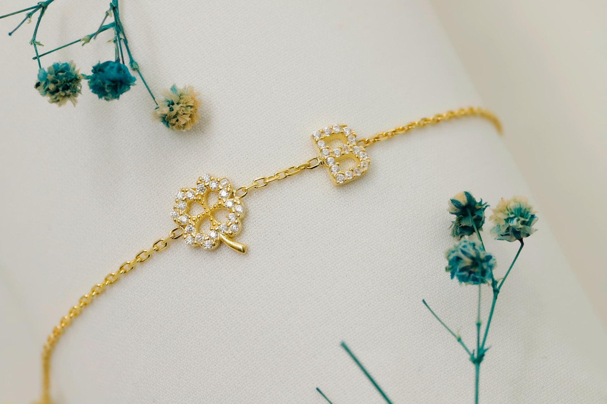Gold bracelet with decorative elements on a mannequin arm, surrounded by small blue flowers.