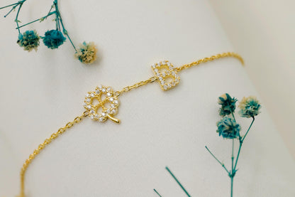 Gold bracelet with decorative elements on a mannequin arm, surrounded by small blue flowers.