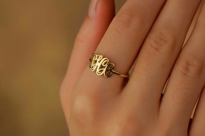 A person's hand displaying a gold-filled monogram ring on the ring finger.