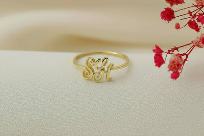 Gold ring with 'S&H' on a beige surface with pink flowers