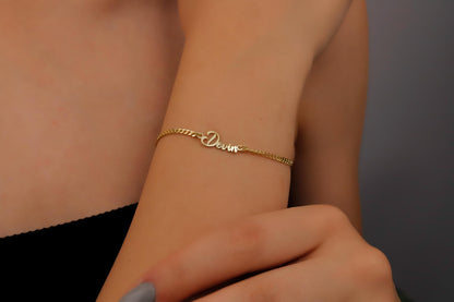 A close-up image of a person wearing a personalized name bracelet with a chain link design in silver.