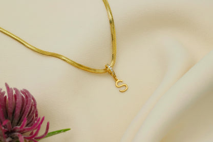 Gold necklace with a 'S' pendant on a beige background