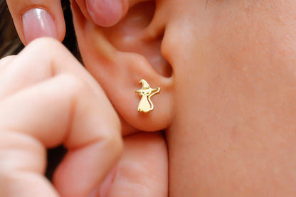 A close-up image of a person's ear wearing a gold-colored stud earring in the shape of a cat.