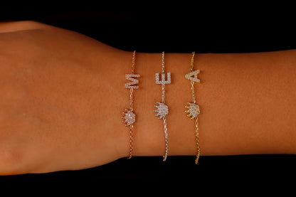 A series of three dainty bracelets worn on a wrist, featuring initials and crown charms with cubic zirconia stones.