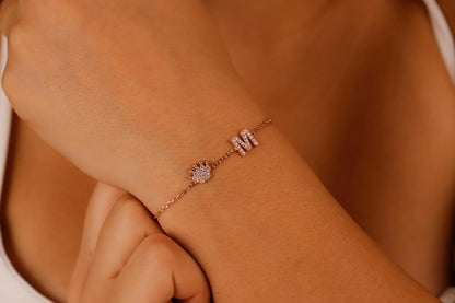 A  dainty bracelet worn on a wrist, featuring initials and crown charms with cubic zirconia stones.