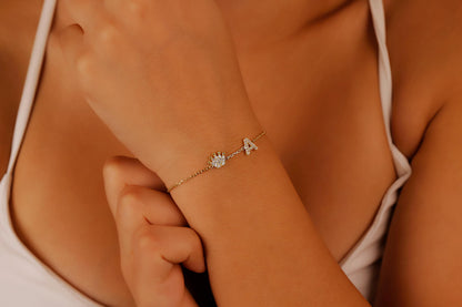 A  dainty bracelet worn on a wrist, featuring initials and crown charms with cubic zirconia stones.