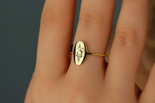 Gold ring with a design on a person's finger against a neutral background