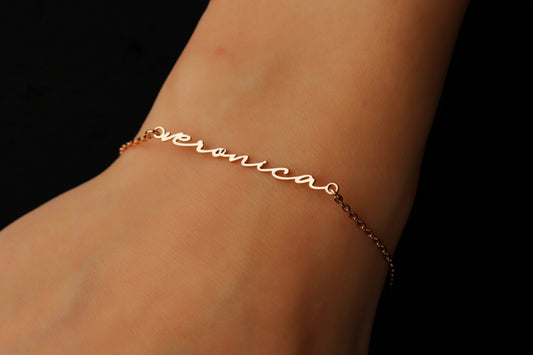 Gold bracelet with 'veronica' engraving on a wrist against a black background