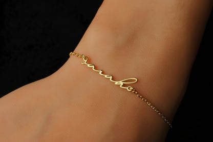 Gold bracelet with 'Natalie' engraved on a wrist against a black background