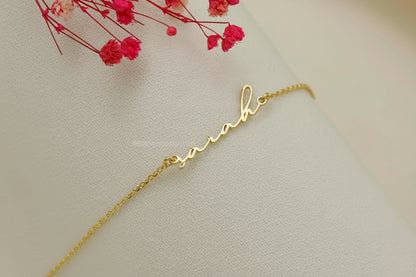 Gold bracelet with a cursive 'love' design on a light background with red flowers.