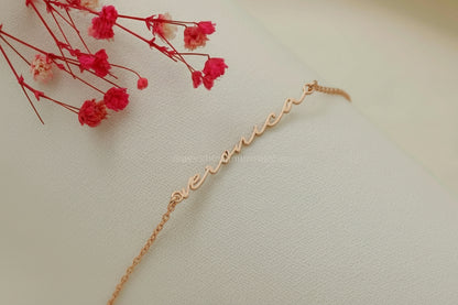 Gold bracelet with 'love' engraving next to red flowers on a light background