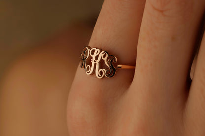 Gold monogram ring on a person's finger with a warm, blurred background