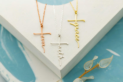 Three cross-shaped necklaces in gold, silver, and rose gold on a white stand with a blue background.