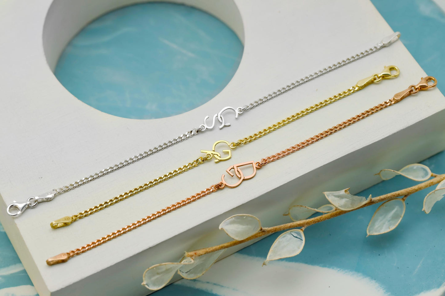 Three gold bracelets on a white stand with a blue background
