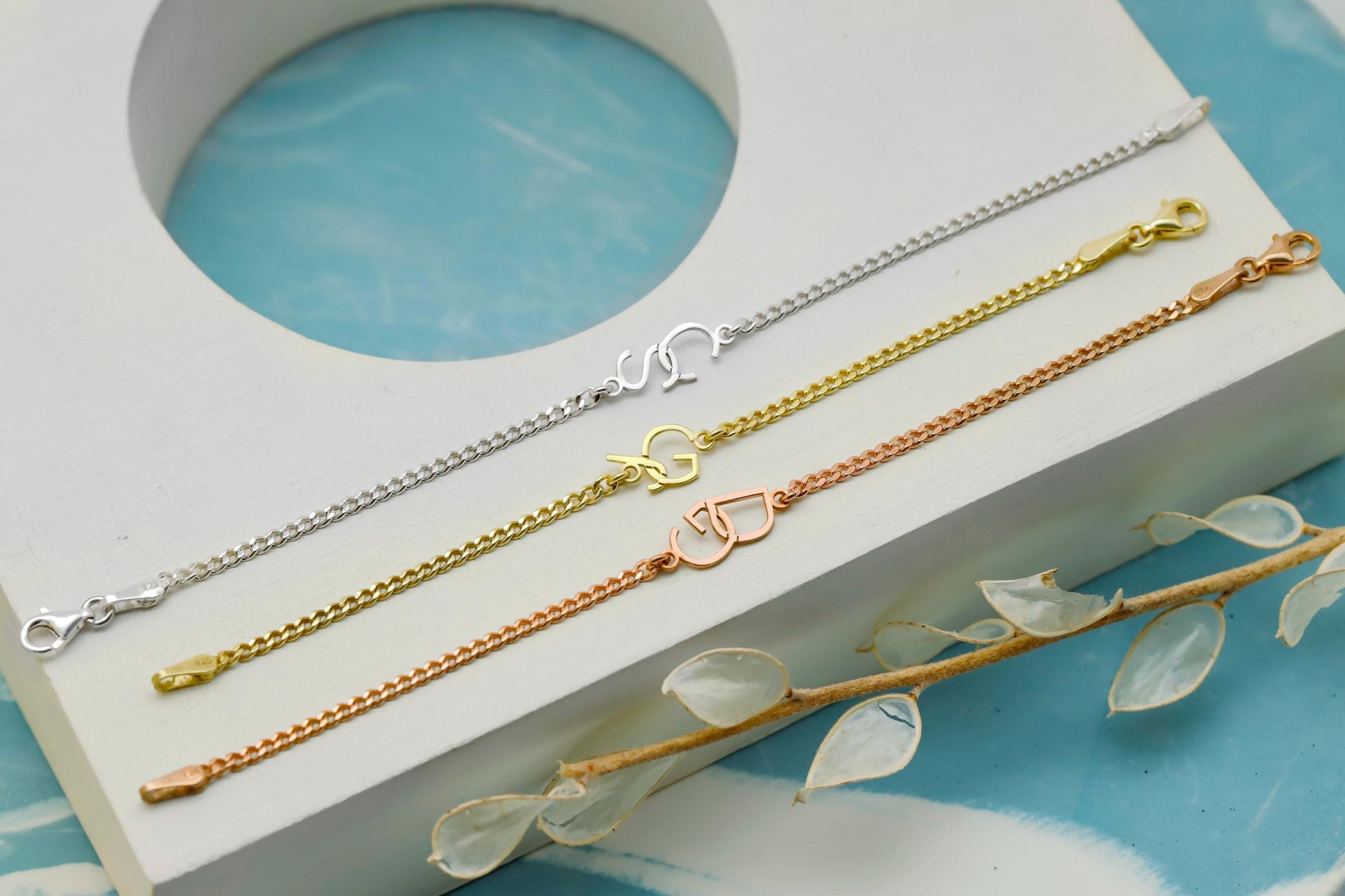Three gold bracelets on a white stand with a blue background