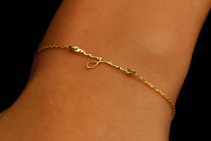 A close-up image of a gold personalized name bracelet on a person's wrist, featuring a delicate chain design and a custom initial pendant.
