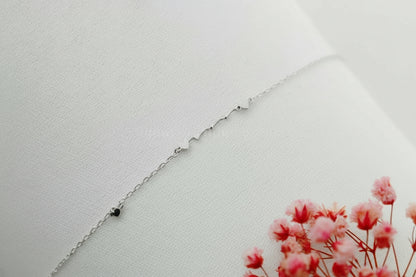 Silver necklace on a light gray background with pink flowers in the corner