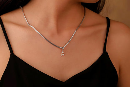 A person wearing a black tank top showcasing a gold-filled snake chain necklace with a initial pendant in the shape of the letter 'R'.