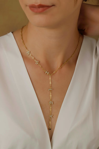 A woman wearing a white v-neck top and showcasing a gold-colored lariat y-shaped necklace with sparkling stones.