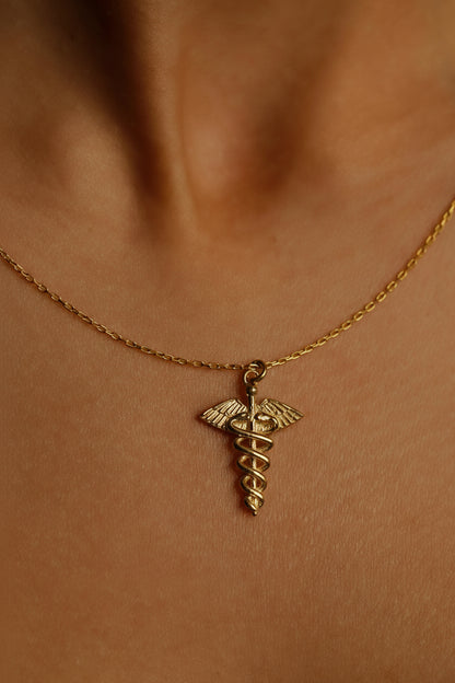 Gold necklace with a caduceus pendant on a person's neck