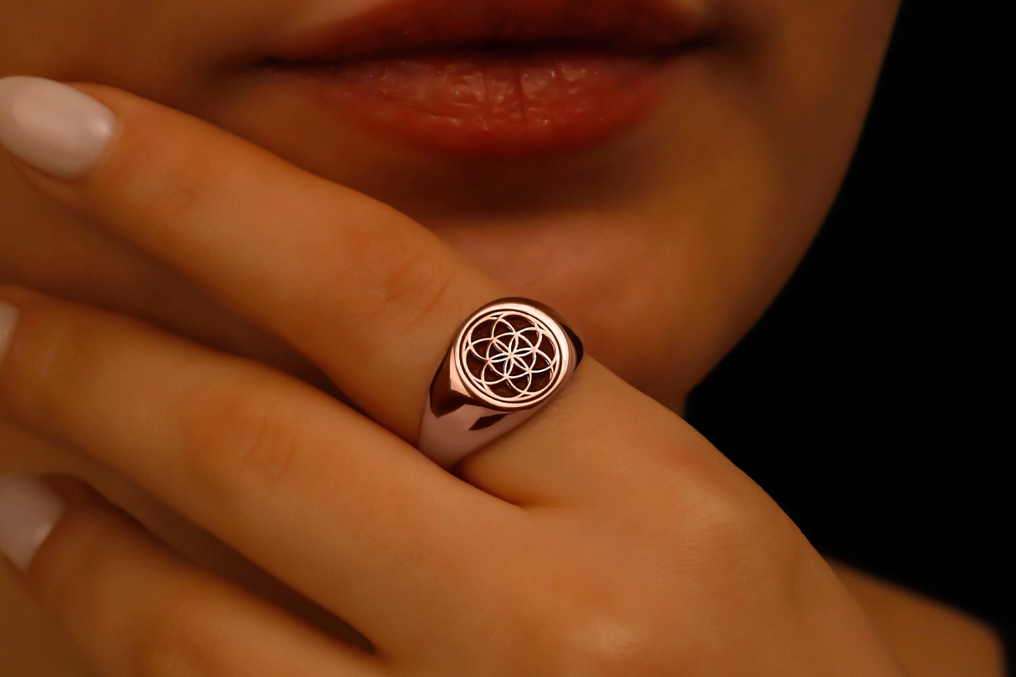 Rose gold ring with a symbol on a hand against a dark background