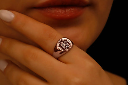 Rose gold ring with a symbol on a hand against a dark background