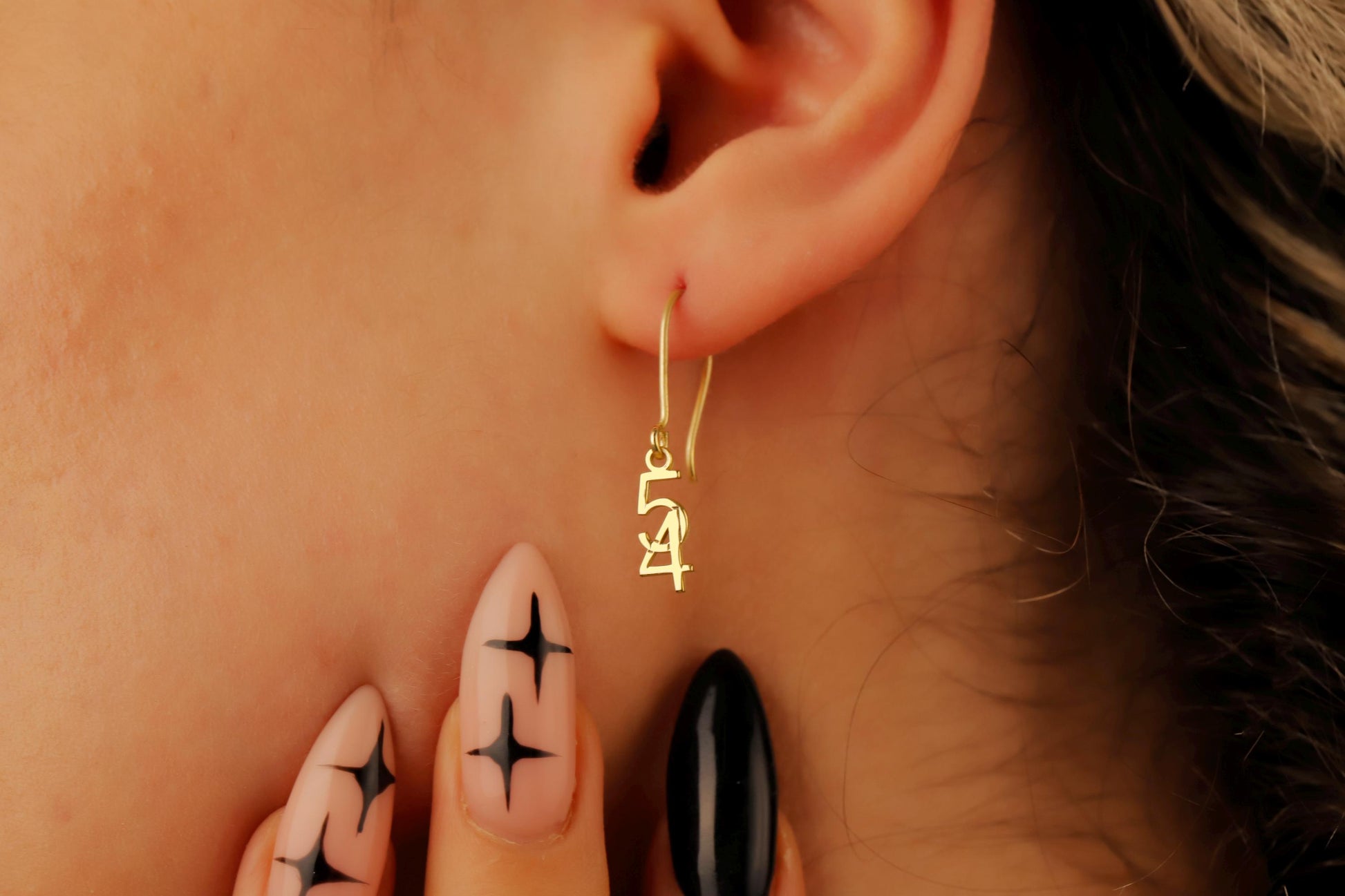 Close-up of an ear wearing a gold hoop earring with intricate designs, surrounded by skin and a blurred background.