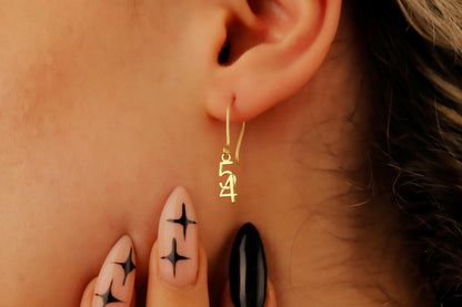 Close-up of an ear wearing a gold hoop earring with intricate designs, surrounded by skin and a blurred background.