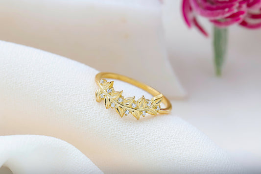 Gold ring with floral design on a white surface with a pink flower in the background